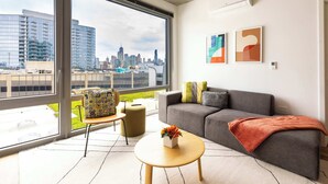 A modern living room with a large window, a grey sofa, a round coffee table, and two abstract paintings on the wall.