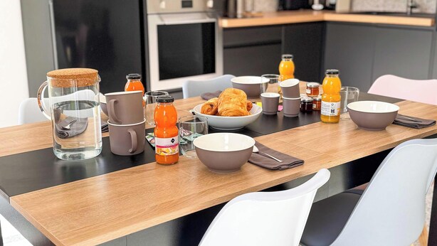 Colazione servita con un boccale d'acqua, succo d'arancia e croissant su un tavolo di legno.
