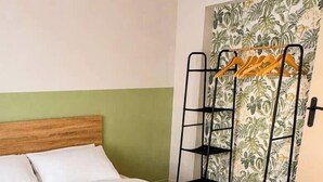 Un letto singolo con testiera in legno, una scaffalatura metallica nera con vestiti e una tenda decorata.