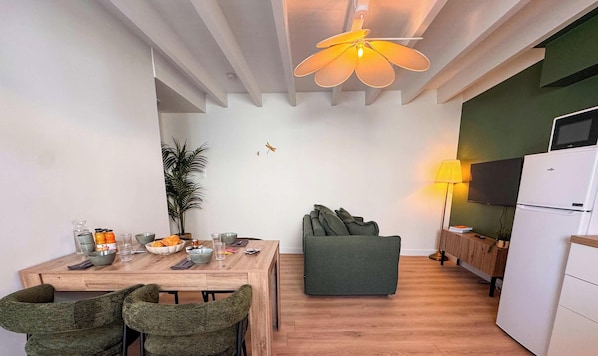 A compact living space with a dining area, a sofa, a TV, and a refrigerator. - Tranquiloue - Nid Douillet - 15min Puy du Fou (Les Herbiers)
