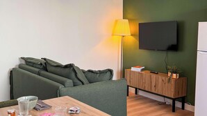 Moderni olohuone, jossa on sohva, puinen sohvapöytä, litteänäyttöinen televisio, kattotuuletin ja vihreä tehosteseinä.