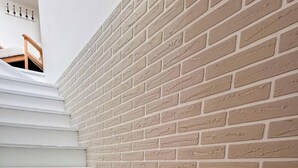 Valkoisista portaista koostuva portaikko johtaa huoneeseen, jonka seinä on tehty tiilistä.