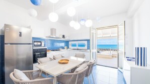 A modern kitchen with a view of the sea, a dining area with wicker chairs, and a large window. - Amira Beach Villa by LeDhome (Trappeto)