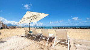 A beachside seating area with a large umbrella, wooden deck, and ocean view. - Amira Beach Villa by LeDhome (Trappeto)