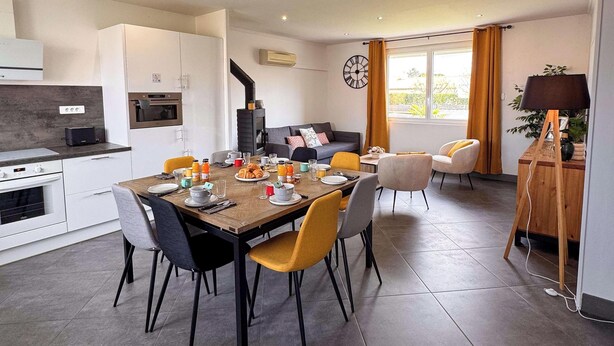 A modern kitchen with a dining area, a built-in stove, and a clock on the wall. - Tranquiloue - Maison 8 Pers - 15 min Puy du Fou (Les Herbiers)