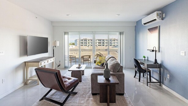 Una sala de estar moderna con sofá, mesa de centro y sillas, un televisor de pantalla plana y un ventanal con vistas a la ciudad.
