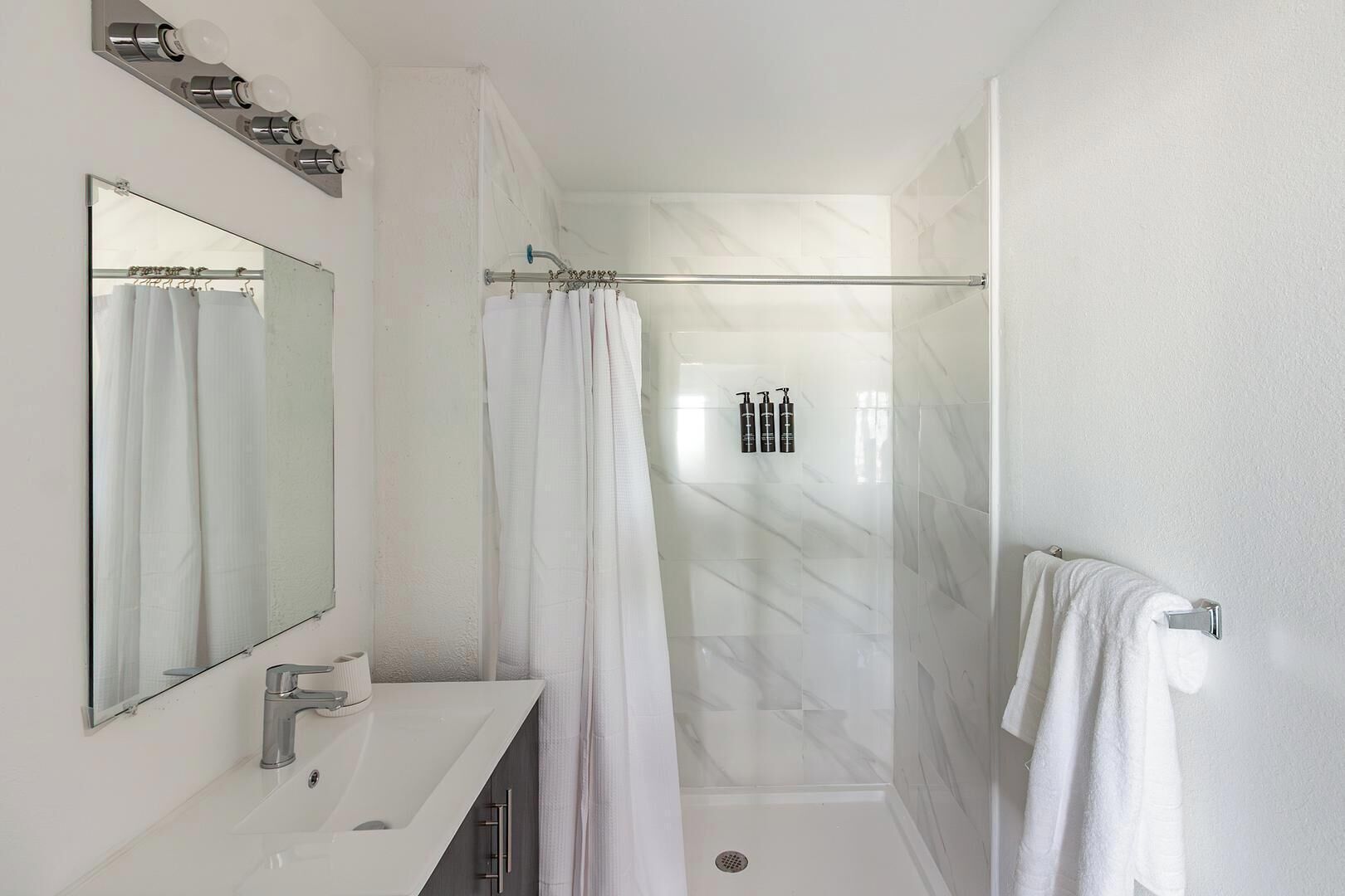 A modern bathroom with a large mirror, white vanity, shower with glass doors, and a towel rack.