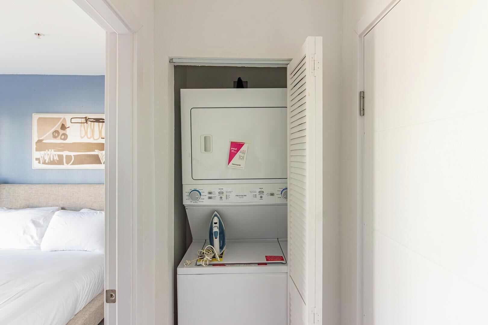 Une chambre d’hôtel de taille réduite, comprenant un lit, un petit coin buanderie et une planche à repasser fixée au mur.
