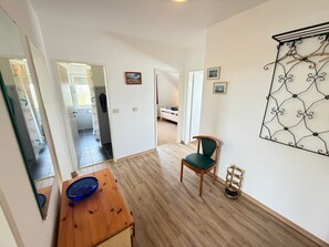 Una habitació amb sòl de fusta, una cadira, un taulell amb un bol blau, una prestatgeria de metall penjada a la paret i una porta que dona a una altra habitació.