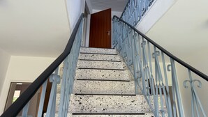 Una escalera con barandilla de metal, una puerta de madera en la parte superior y un techo con textura.