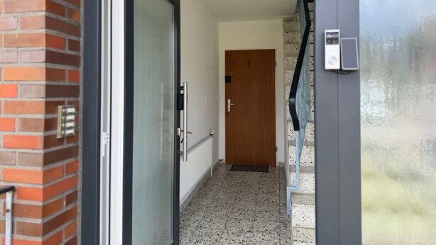 Un pasillo con puerta de vidrio, puerta de madera, radiador y escalera.