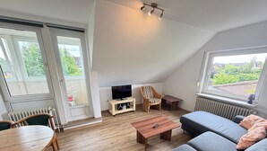 Una sala de estar acogedora con un sofá, un televisor sobre un mueble bajo, una silla, una mesa y vistas a espacios verdes.