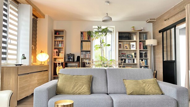 Un salón con un sofá gris, una mesa de centro de madera y una estantería llena de libros y objetos decorativos.