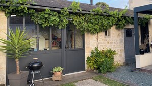Una casa con un porche techado, una ventana a la vista, una puerta, un pequeño jardín y una parrilla.