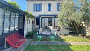 Una casa con un patio, dos sillas verdes, una silla roja y una parrilla.