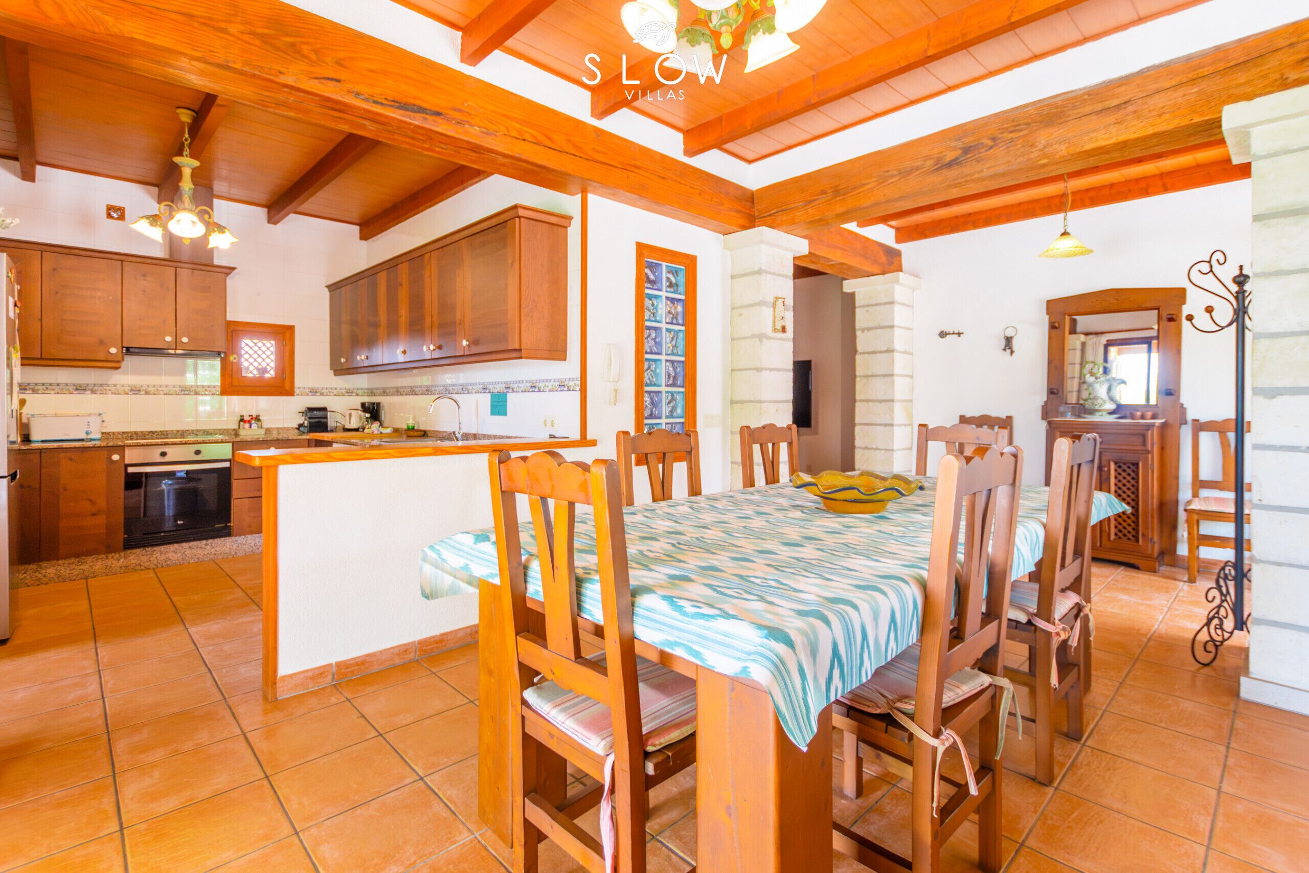 A kitchen with wooden cabinets, a central island, and a dining area with wooden chairs and a table.