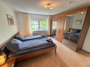 A bedroom with two beds, a wardrobe, a window with curtains, and a radiator.