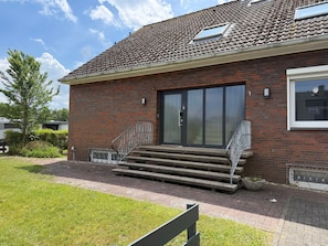 A brick building with a tiled roof, a large sliding glass door, and a set of concrete steps leading to the entrance.