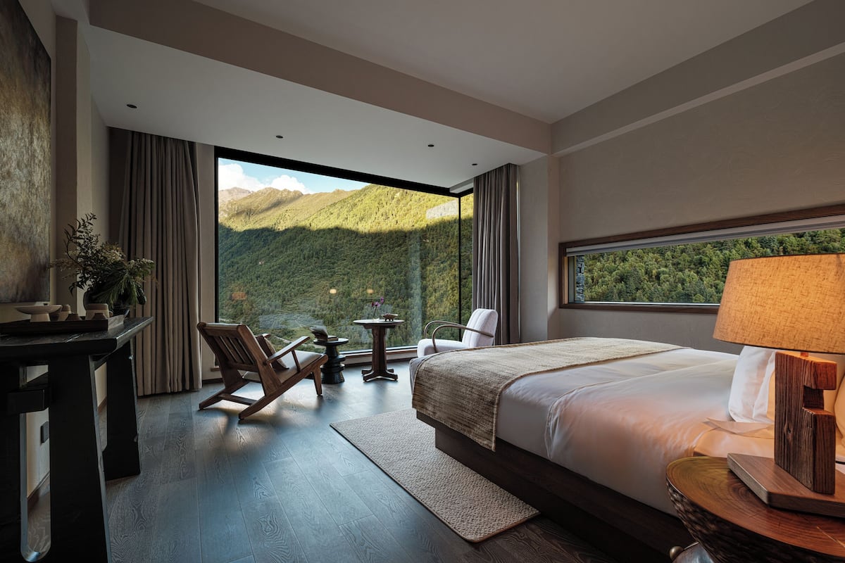 Ein modernes Hotelzimmer mit einem großen Bett, einem Schreibtisch, einem Stuhl und Blick auf Berge.