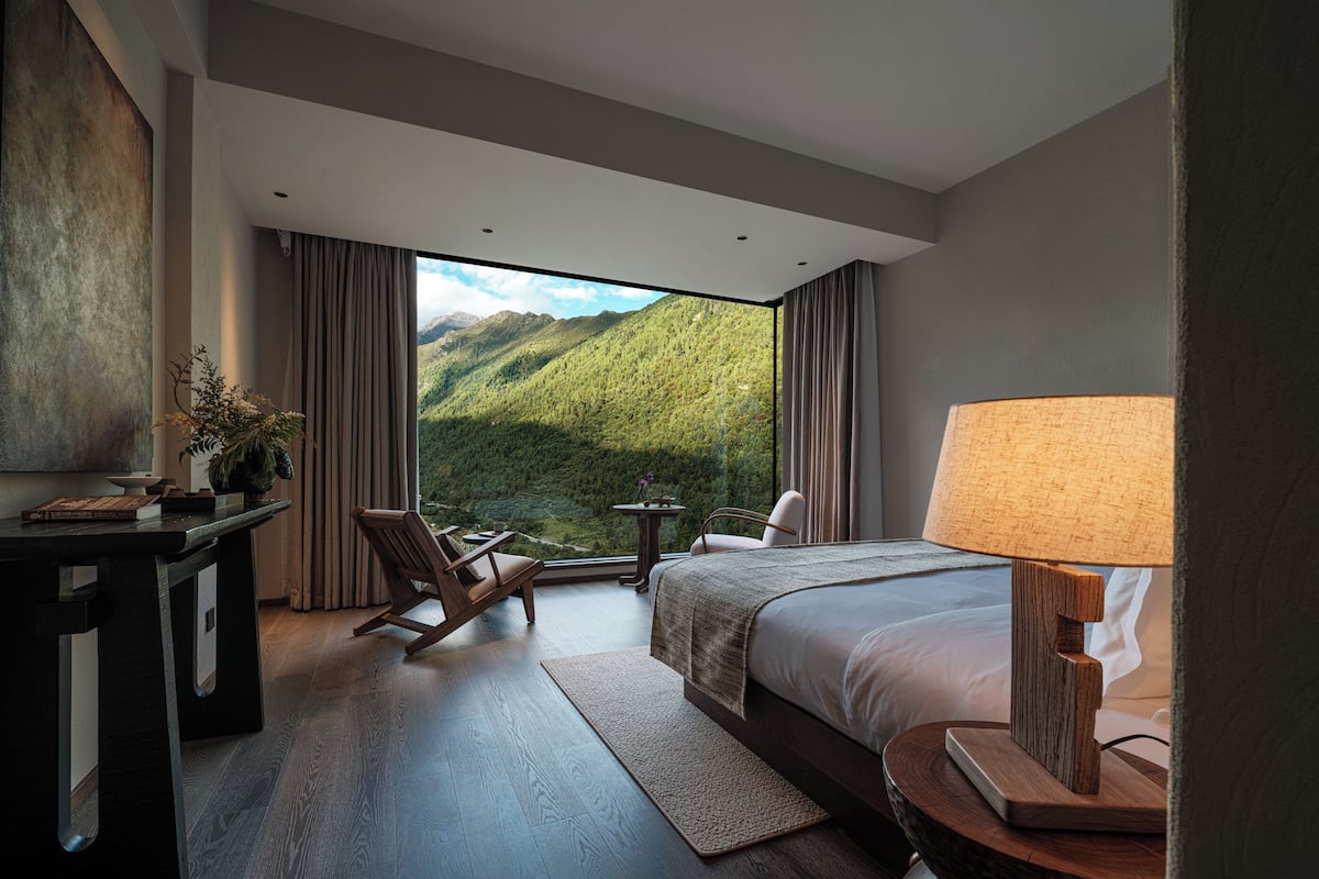 Ein modernes Hotelzimmer mit einem großen Bett, einem Schreibtisch, einem Stuhl und Blick auf Berge.