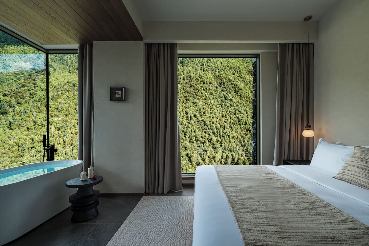 Ein Schlafzimmer mit großem Fenster, einem Bett, einem kleinen Tisch mit einer Flasche und einem Wandbild.