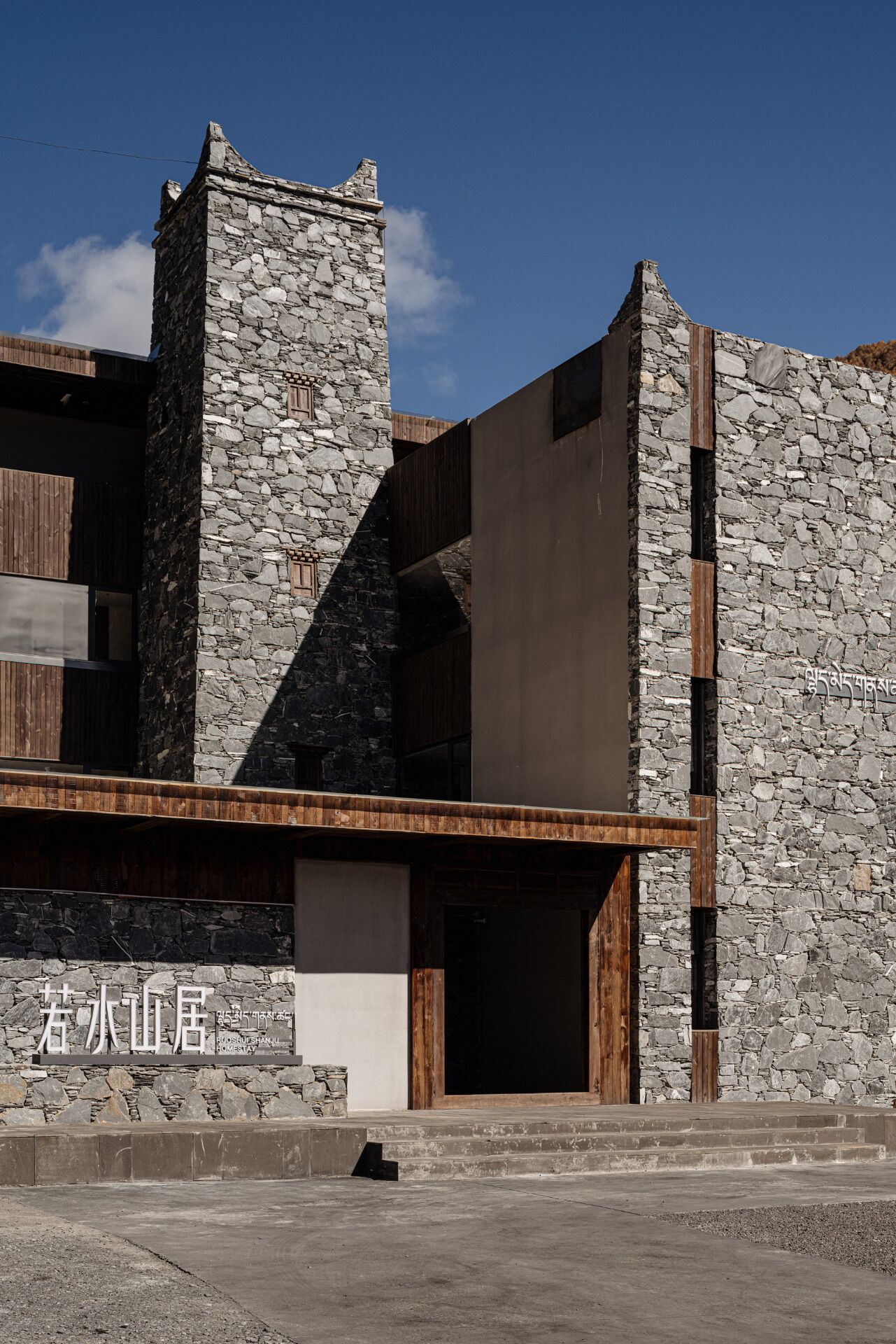 Un edificio moderno con muros de piedra y detalles de madera, que presenta una entrada amplia y una escalera que conduce a la entrada principal.