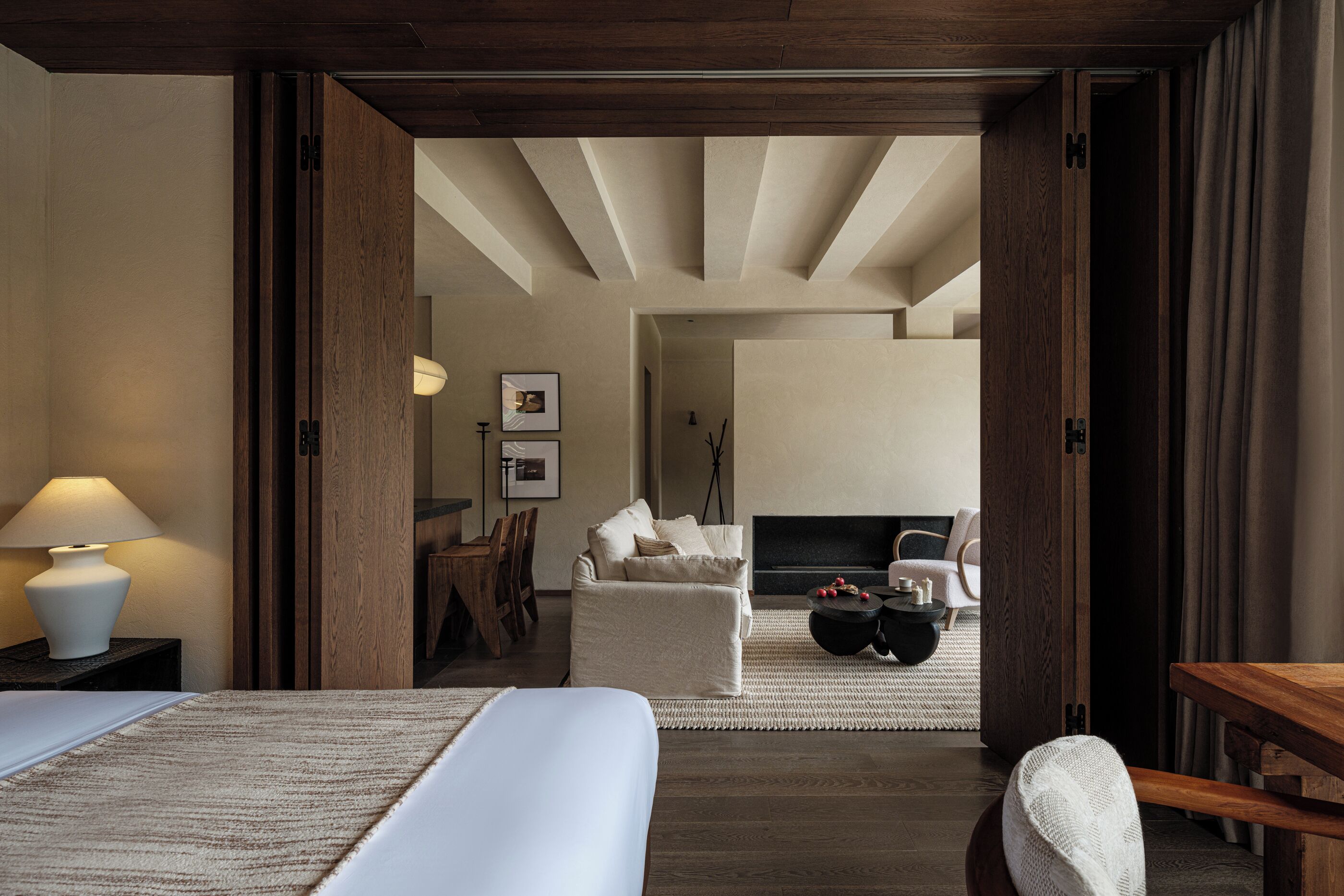 Habitación de hotel con una cama, una puerta de madera, una mesita, una silla, un sofá, una chimenea y una lámpara.