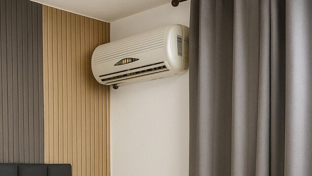 A bed with a quilted cover, a wall-mounted air conditioner, and a curtain.