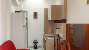 A compact living space with a kitchenette, a dining area with wooden chairs, a red sofa, and a small refrigerator.