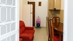 A compact living space with a dining area, a red sofa, wooden chairs, a refrigerator, and a water dispenser.