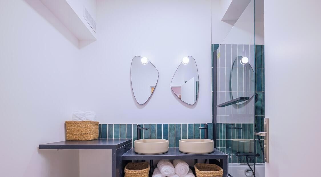 A modern bathroom with two round sinks, a towel rack, and a mirror with lights.