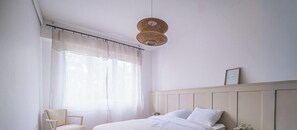 Ein Schlafzimmer mit einem Bett, einem Sessel, einer Hängelampe und einem gerahmten Bild an der Wand.