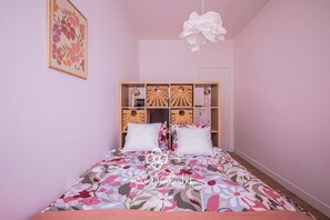 Ein Schlafzimmer mit floralem Bettbezug, einem hölzernen Kopfteil mit Stauraum und einer Pendelleuchte.