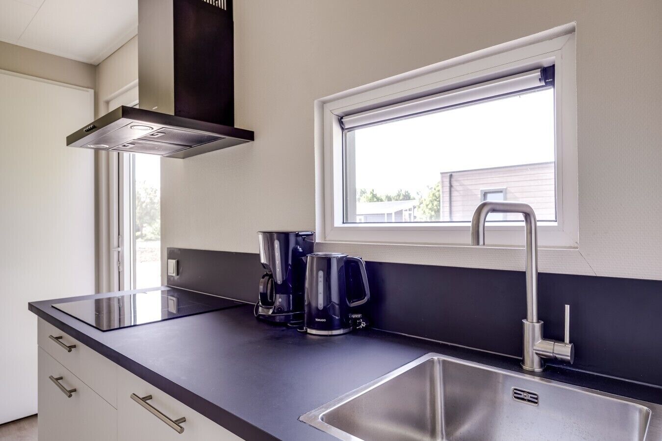 Een moderne keuken met een zwart aanrecht, een roestvrijstalen spoelbak en een raam met uitzicht.