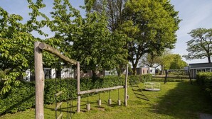 A playground with wooden climbing structures and swings, surrounded by lush green grass and trees.