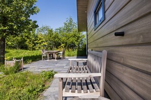 A wooden deck with a bench and a table, surrounded by greenery and trees.