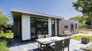 A modern outdoor patio with a table and chairs, a wooden deck, and a building with large glass doors.