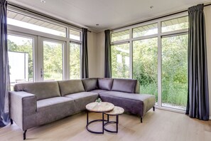 A modern living room with a sectional sofa, a round coffee table, and large windows with curtains.