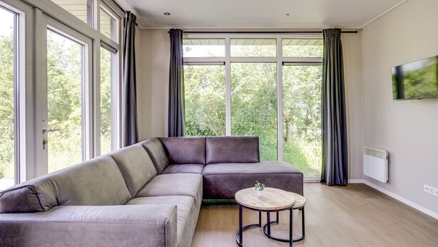 A modern living room with a sectional sofa, a round coffee table, and large windows with curtains.