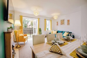 A dining area with a table set for two, a sofa, and a television in the background. - Central Cactus Luxurious Home | Free Parking 10PPL (Sheffield)