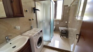 A bathroom with a washing machine, a sink, a toilet, and a shower area. - Apartment Sleeps 3 - Private Garden - Pets Welcome (Realmonte)