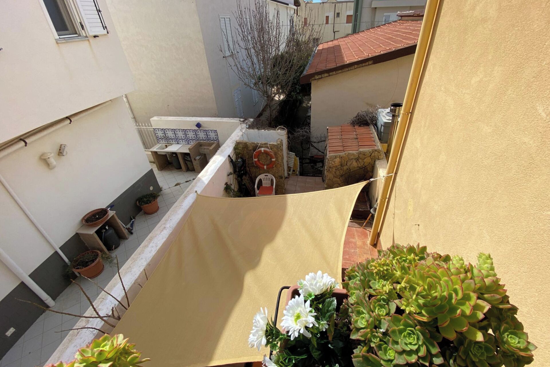 A narrow courtyard with a stone wall, a small table, and potted plants.