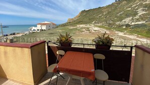 A balcony with a table and chairs, overlooking a beach and a white building with a red roof. - Apartment Sleeps 3 - Private Garden - Pets Welcome (Realmonte)
