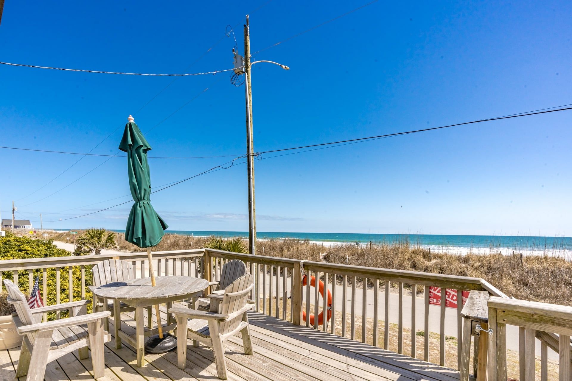 A wooden deck with a table and chairs, overlooking a beach with a clear sky.