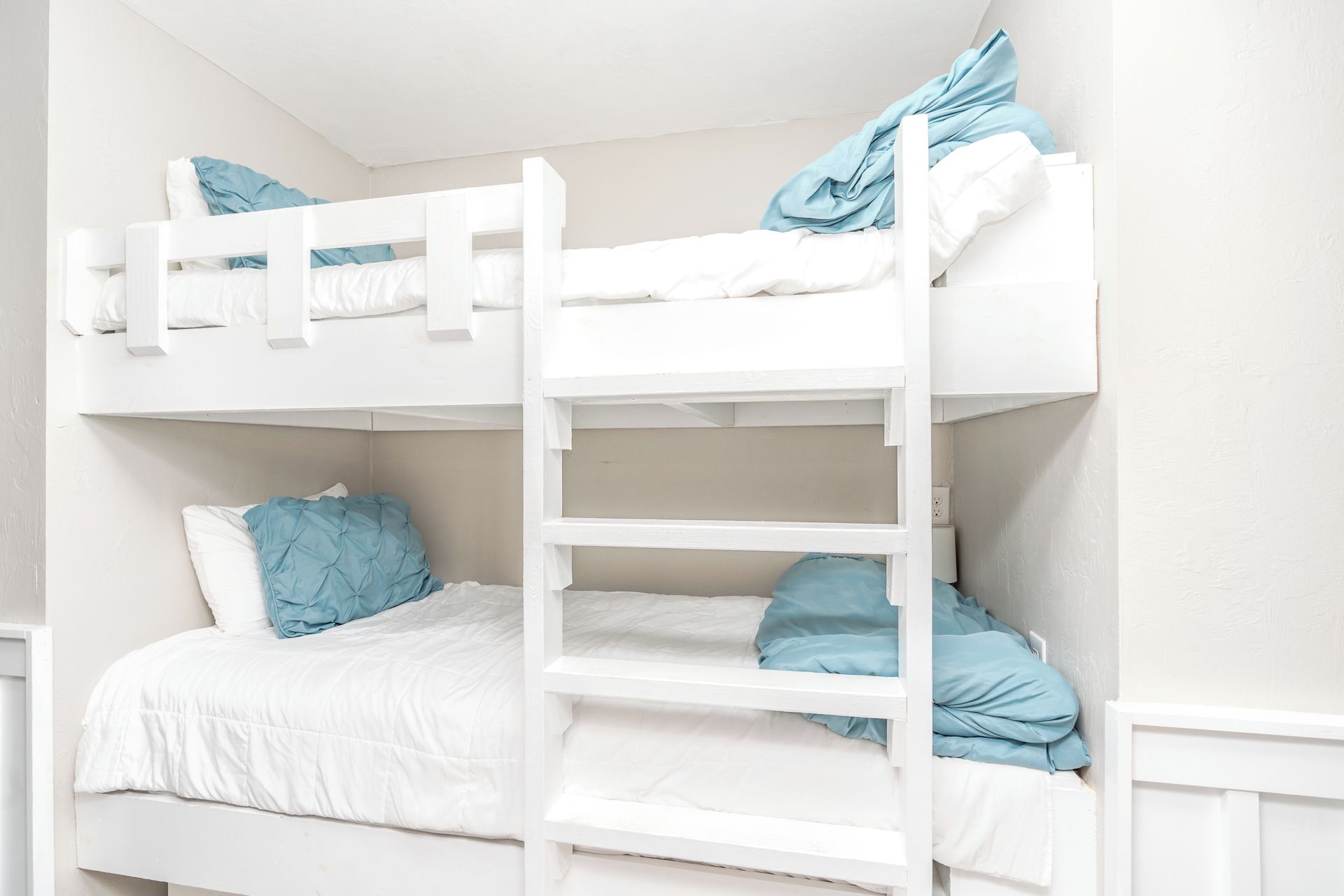 Un lit superposé avec une échelle, du linge de lit blanc et des oreillers bleus.