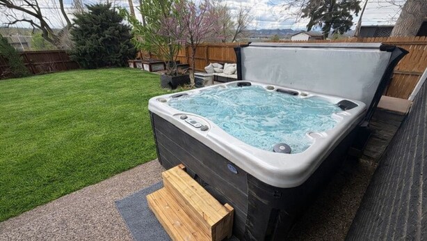 A hot tub with a wooden step leading up to it, surrounded by a backyard with a lawn and trees. - Backyard Escape + Hot Tub - Minutes to Red Rocks & Denver-Large Basement Hangout (Arvada)