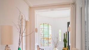 Un passadís amb una làmpada, branques despullades, una finestra de vitralls i un cactus.