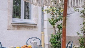 Exterior d'un edifici amb una finestra, una taula i cadires, i una planta.