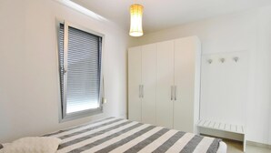 Un dormitorio con cama, armario, banco y ventana con persianas.