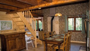 A wooden staircase, a dining table with chairs, a stone wall, and a window with a view of trees. - Le P'tit Chalet, at 1000m altitude (Campan)